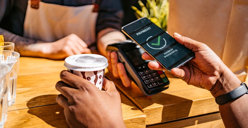 Woman paying via contactless channel by mobile banking application for coffee in coffee shop.