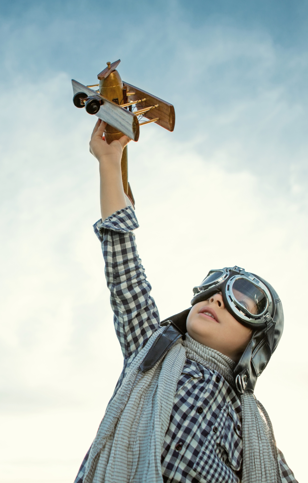 child with aviator helmet flying a toy plane