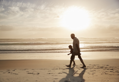 Grandfather with grandchild walking on a beach at sunset